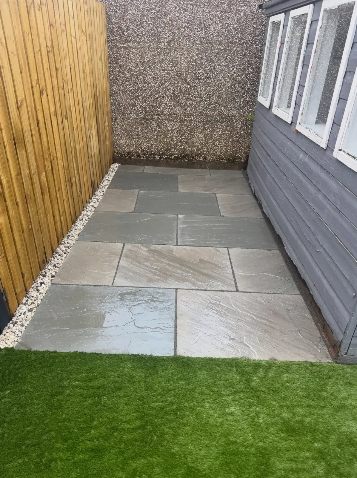 New slate patio with wooden fencing and artificial grass