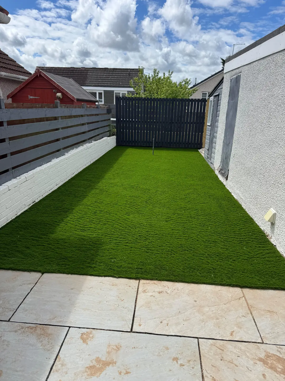Artificial lawn with painted brick wall and slate fence